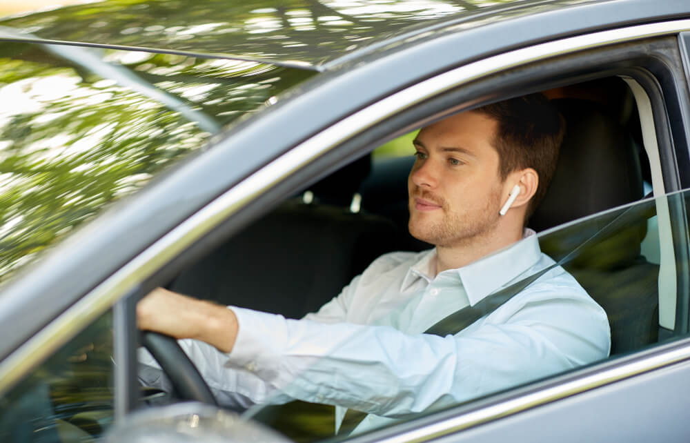 Man driving a car while wearing a wireless earpiece, illustrating hands-free driving laws that allow drivers to use voice-activated or hands-free technology while keeping their hands on the wheel.