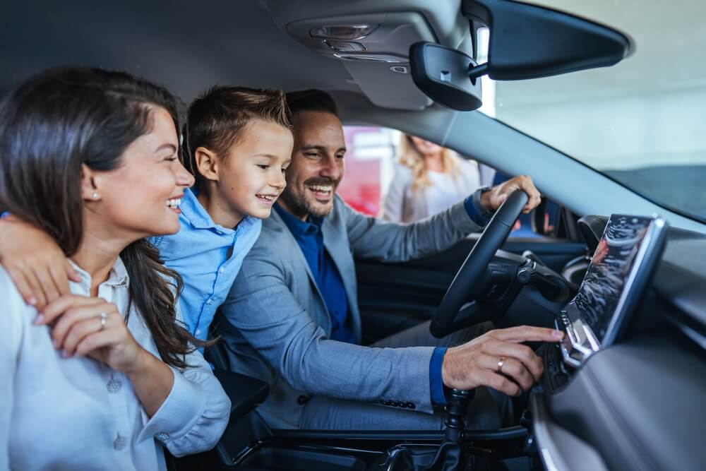 Family sitting in a vehicle and using the car’s touchscreen display, illustrating hands-free driving laws and the use of integrated technology designed to minimize driver distraction. 