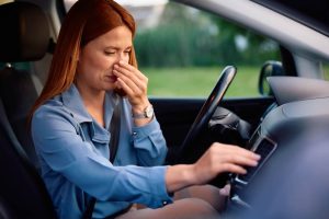 Driver reacting to a musty smell from the car AC while adjusting the air conditioning controls.