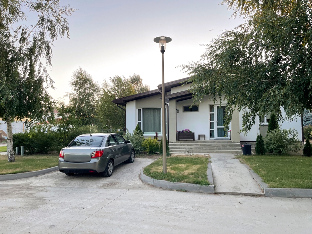 Gray car parked in the driveway of a suburban home surrounded by trees.