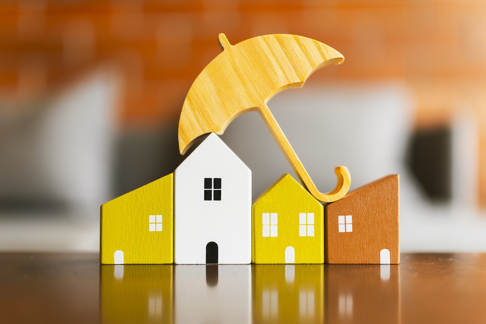Wooden model townhouses protected by an umbrella, representing townhouse insurance coverage.