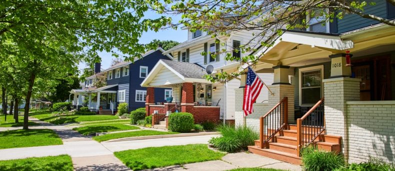 Row of townhouses with front porches, green lawns, and trees in a residential neighborhood.