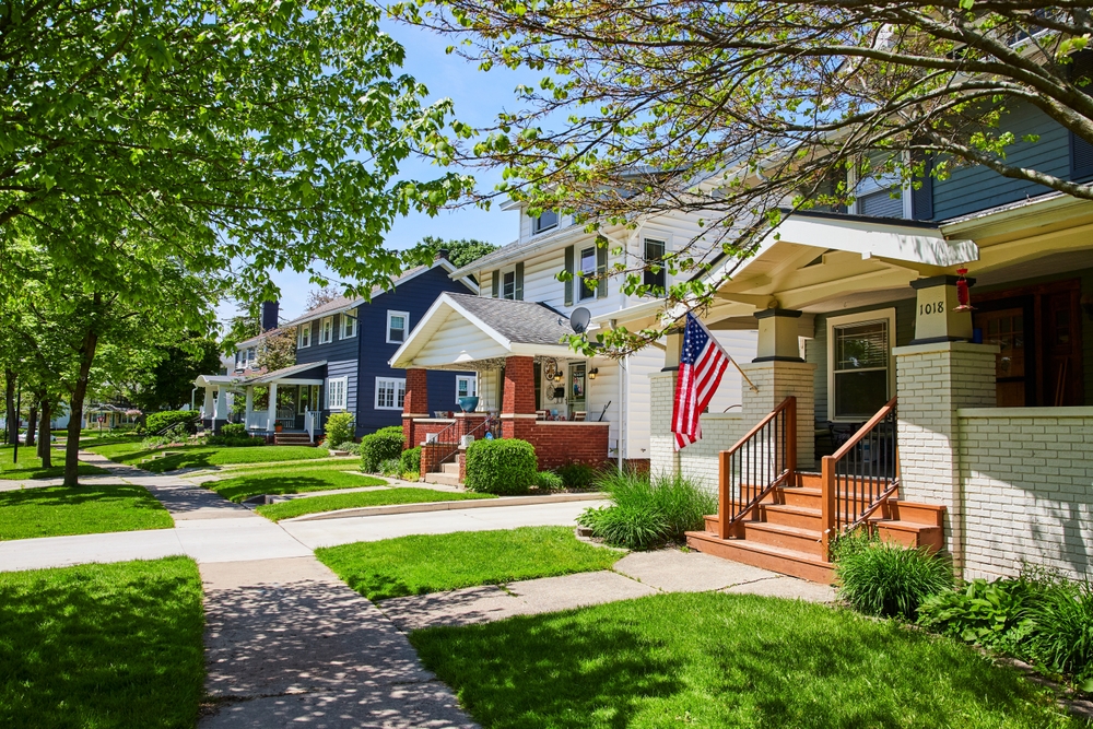 Row of townhouses with front porches, green lawns, and trees in a residential neighborhood.