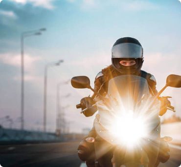 Front view of a man riding his motorcycle with the headlight on