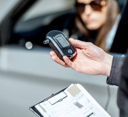 Hand with a breathalyzer with a woman in a car in the background