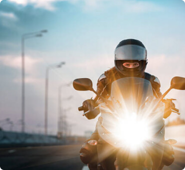 Front view of a man riding his motorcycle with the headlight on
