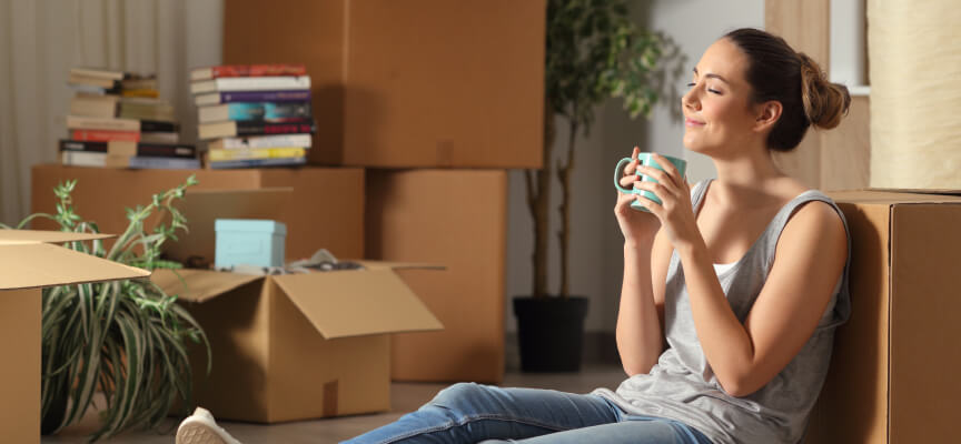 Happy young woman drinking coffee on the floor with moving boxes in the background 