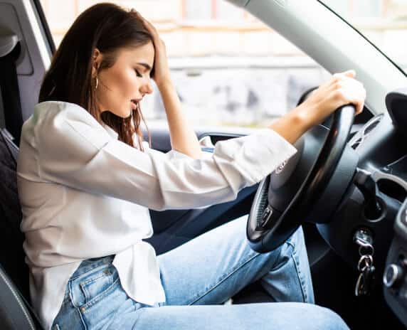 Worried young woman in a cars drivers seat with one hand on her head
