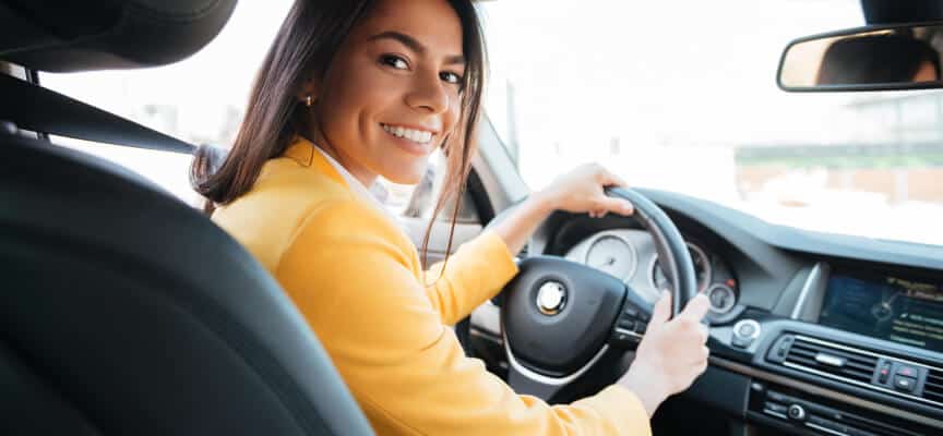 Smiling young hispanic woman in cars drivers seat lookin at the camera