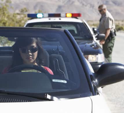 Front view of female driver pulled over with cop and copcar in the background