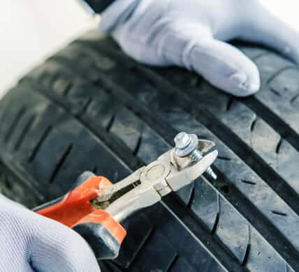 Closeup of hands pulling screw out of tire with pliers