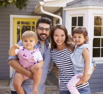 Happy mixed family with two baby girls in front of their home