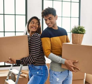 Happy indian couple moving and carriying boxes on new apartment with rentes insurance