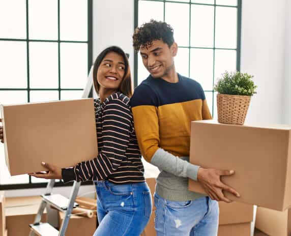 Happy indian couple moving and carriying boxes on new apartment with rentes insurance