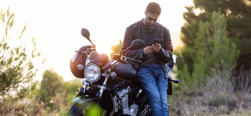 Man leaning on his motorcycle while he looks at his smarphone