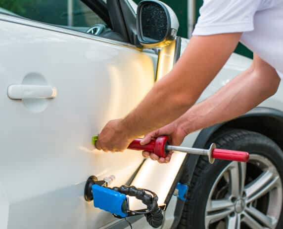 Person fixing a dent in a car using a paintless repair machine