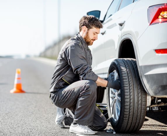 Side view of male mechanic changing a tire on a road