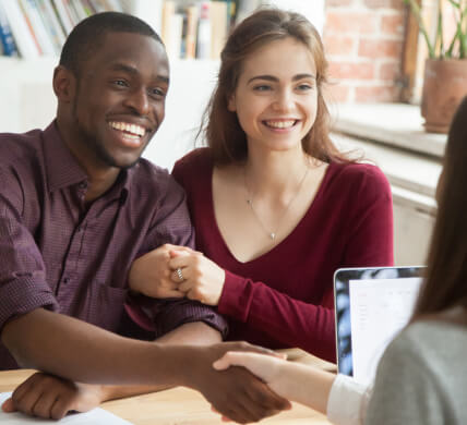 Smiling couple in office with insurance agent shaking hands with the man