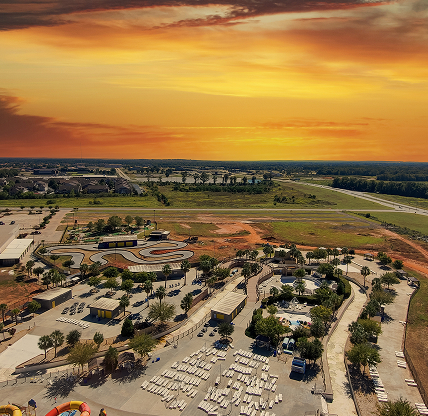 An aerial shot of the city of Warner Robins Georgia with vast miles of lush green trees, grass and plants with buildings and highways with cars driving and powerful clouds at sunset