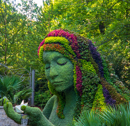 The Earth Goddess covered in colorful flowers surrounded by lush green trees, grass and plants with blue sky at Atlanta Botanical Garden in Atlanta – cheap car insurance in Georgia.