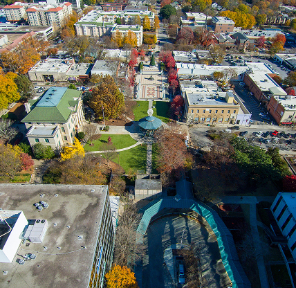 An aerial shot of the office buildings, apartments, city hall, red and yellow autumn trees, lush green trees and grass, Christmas tree and parked cars at Decatur Square in Decatur - cheap car insurance in Georgia.