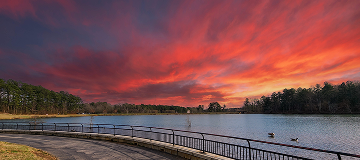 a gorgeous winter landscape at Rhodes Jordan park with a blue lake, yellow winter grass lush green trees, people walking and powerful clouds at sunset in Lawrenceville - cheap car insurance in Georgia.