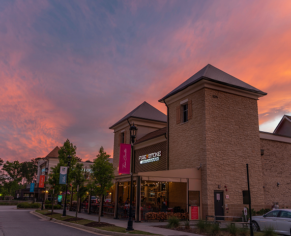 A photo of a bar and grill in a Peachtree Corners shopping center. Setting sun behind colorful clouds in the background.