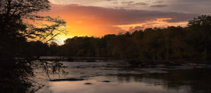 sunrise over the Chattahoochee River in Newnan Georgia surrounded by silhouette of fall foliage, sunlight glistening off river water - cheap car insurance in Georgia.