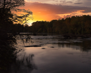 sunrise over the Chattahoochee River in Newnan Georgia surrounded by silhouette of fall foliage, sunlight glistening off river water - cheap car insurance in Georgia.
