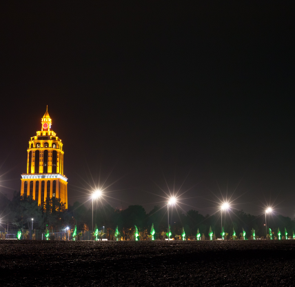 A nighttime skyline scene shows a tall, golden-lit tower rising above a dark park area, with bright streetlights and small green accent lights lining the foreground in Braselton, Georgia. Cheap car insurance in Georgia.