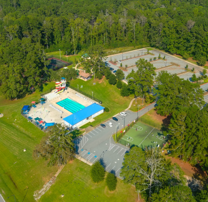 A stunning aerial shot of a parking lot, a pool and a basketball court surrounded by vast miles of lush green trees at Duncan Park in Fairburn Georgia USA