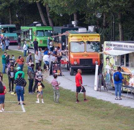 Lilburn, GA USA - October 10, 2023: People stand in line at five food trucks in a public park, on October 10, 2023 in Lilburn, GA.